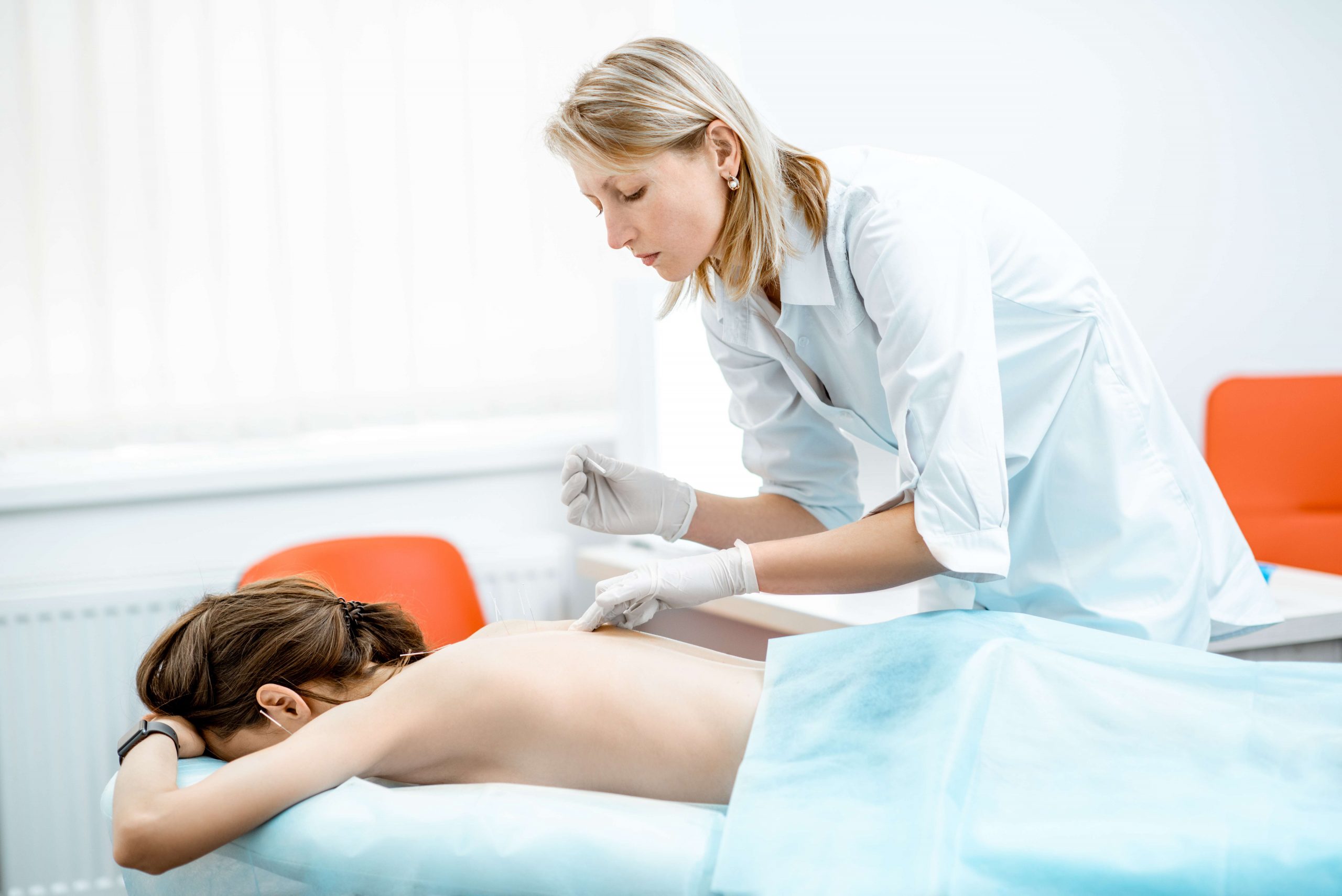 Neuropathologist puts needles into the woman's back removing inflammation of the muscles during the acupuncture treatment in the office